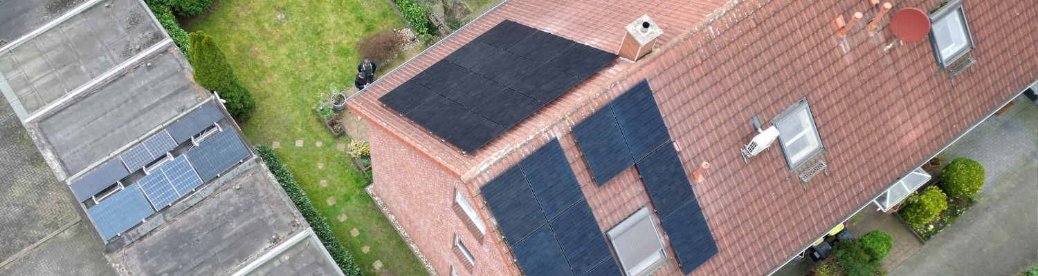 Rotes Dach von oben mit Photovoltaikanlage und einem kleinen Garten in Duisburg.