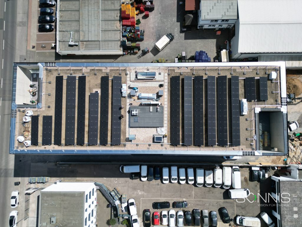 Perspektive von vorne: Geschäftsgebäude mit Solarmodulen, im Hintergrund: weitere Firmengebäude und ein grüner Park