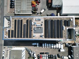 Perspektive von vorne: Geschäftsgebäude mit Solarmodulen, im Hintergrund: weitere Firmengebäude und ein grüner Park