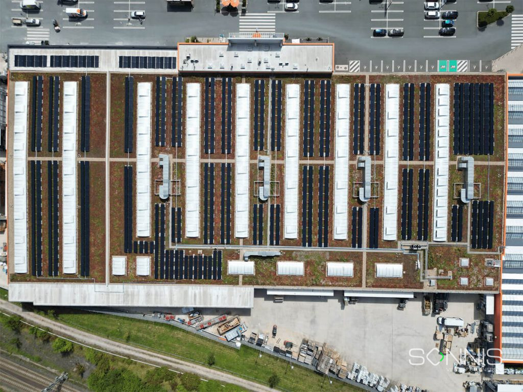 Luftaufnahme einer großen Photovoltaikanlage auf einem begrünten Flachdach.