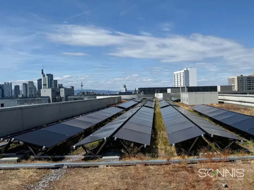 Detailaufnahme der PV-Modulreihen auf einem begrünten Flachdach eines Gewerbegebäudes in Frankfurt; Teil der 200 kWp Anlage von Sonnis Energy mit Skyline im Hintergrund.